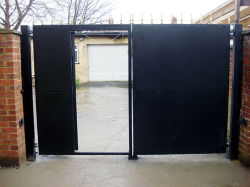 A decorated wrought iron driveway security gate with pedestrian door